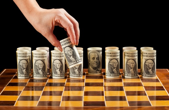 a hand placing rolls of money on a chessboard